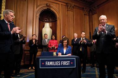 House Speaker Nancy Pelosi, accompanied by House Minority Leader Kevin McCarthy, left, House Majority Leader Steny Hoyer, right, and other legislators, signs the Coronavirus Aid, Relief and Economic Security (CARES) Act after it passed March 27.