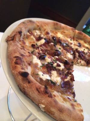 Postrio's caramelized onion pizza comes loaded with bacon, goat cheese, olives and oregano.