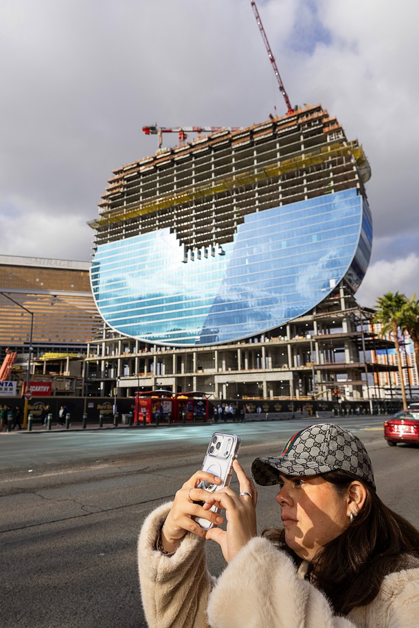 A tourist takes a photo in front of the Hard Rock’s guitar-shaped hotel tower, under construction on the Las Vegas Boulevard South at the site of the Mirage, Friday, Jan. 2, 2026.